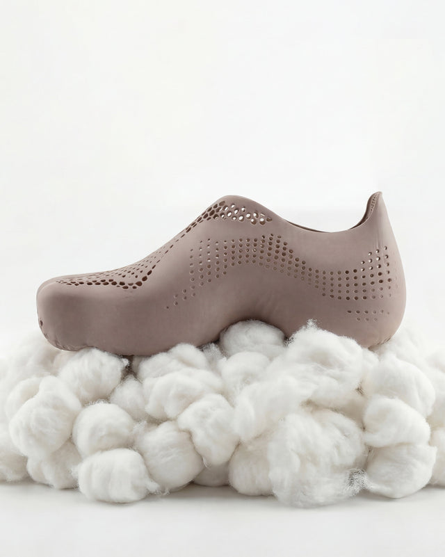 Brown clog shoe on a bed of white cotton with a white background
